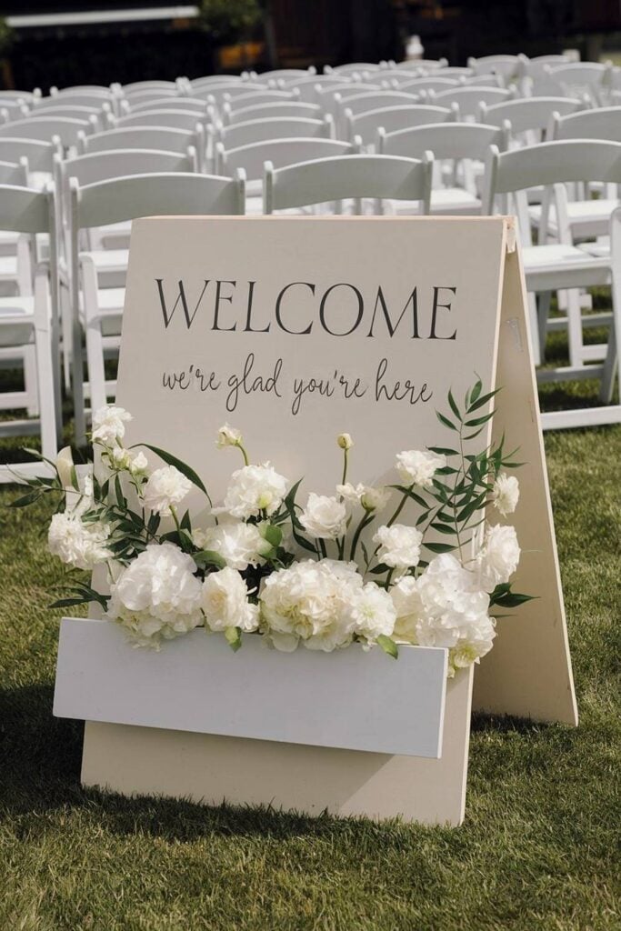 15+ idées de micro-mariages qui transformeront votre espace de cérémonie et de réception image 6 | Soirée Blanche Panneau de bienvenue avec fleurs blanches et verdure au micro-mariage.