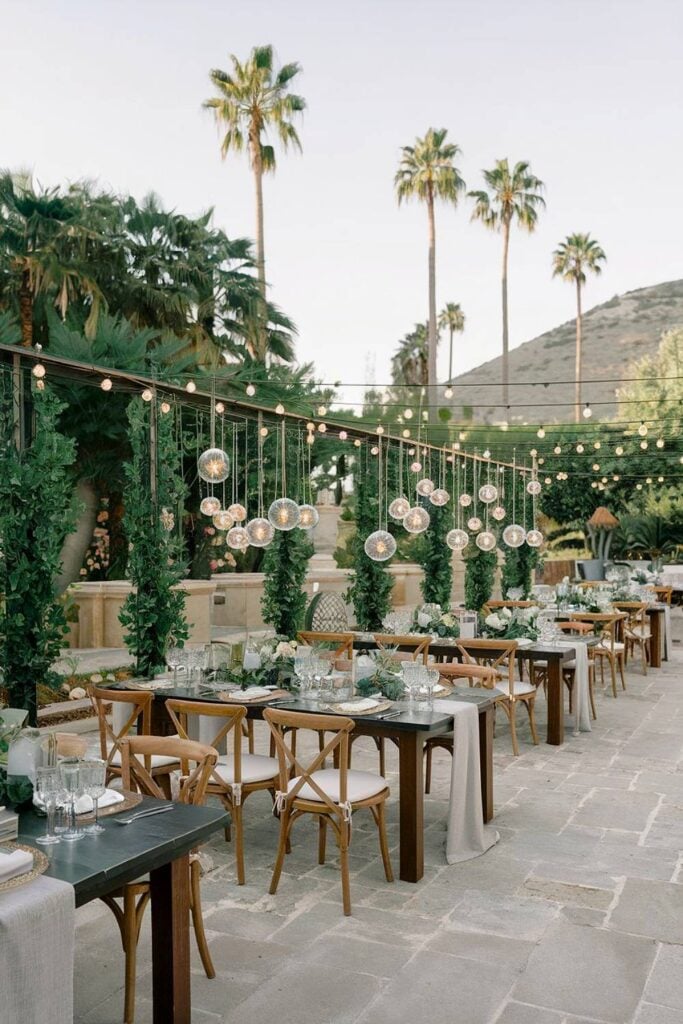 15+ idées de micro-mariages qui transformeront votre espace de cérémonie et de réception image 16 | Soirée Blanche Configuration de mariage dans le jardin avec de la verdure et des globes lumineux suspendus pour un micro-mariage.