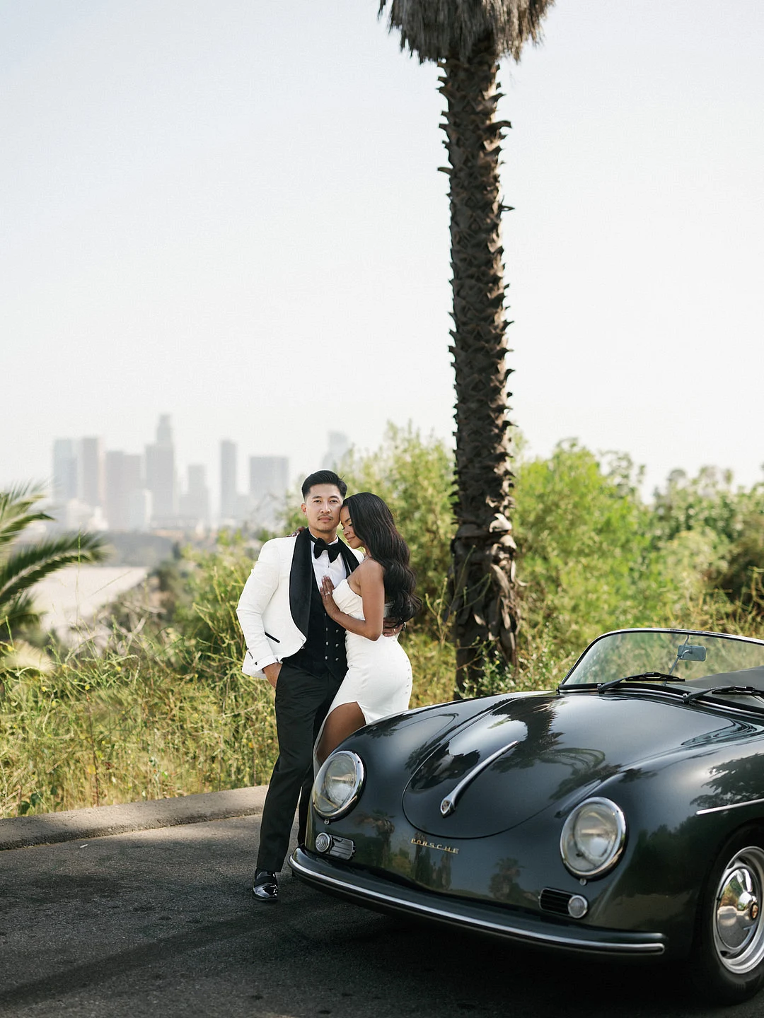 Un mariage glamour sur le toit de Los Angeles avec une Porsche vintage image 19 | Soirée Blanche Un baiser à côté de la voiture dans une rue bordée de palmiers à Los Angeles