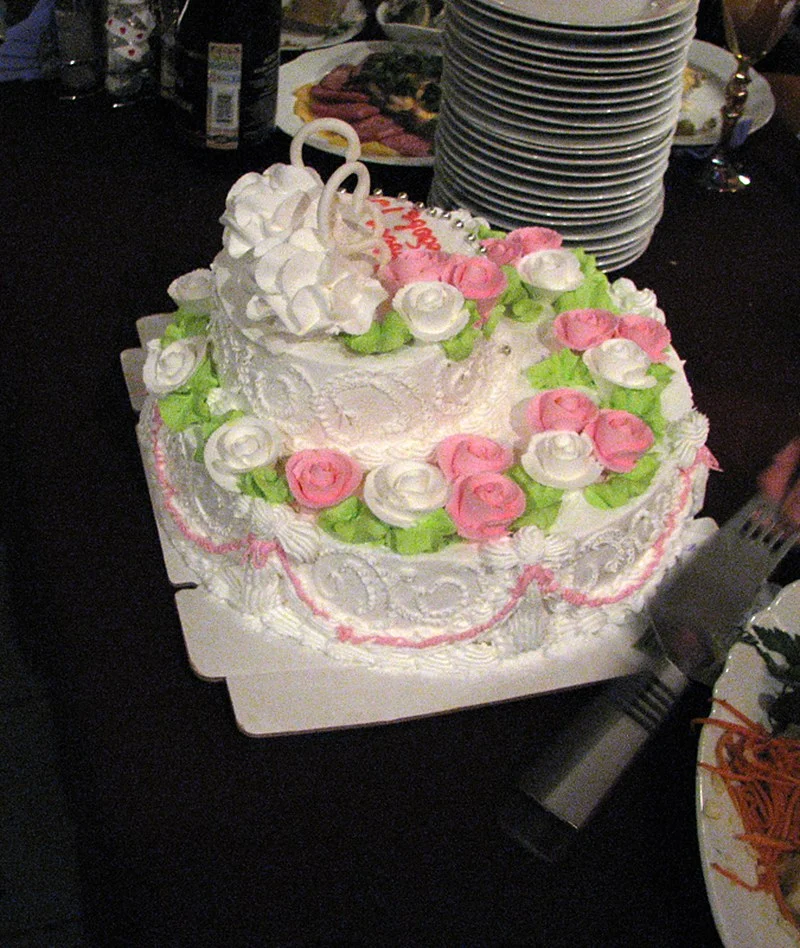Gâteau de mariage blanc recouvert de bordures de glaçage royal ébouriffées, de rideaux roses, de feuilles vertes et de roses crème au beurre passepoilées