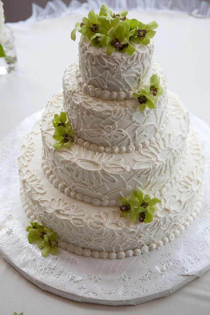 Gâteau de mariage moderne à trois niveaux recouvert de dentelle crème au beurre passepoilée avec des orchidées vertes