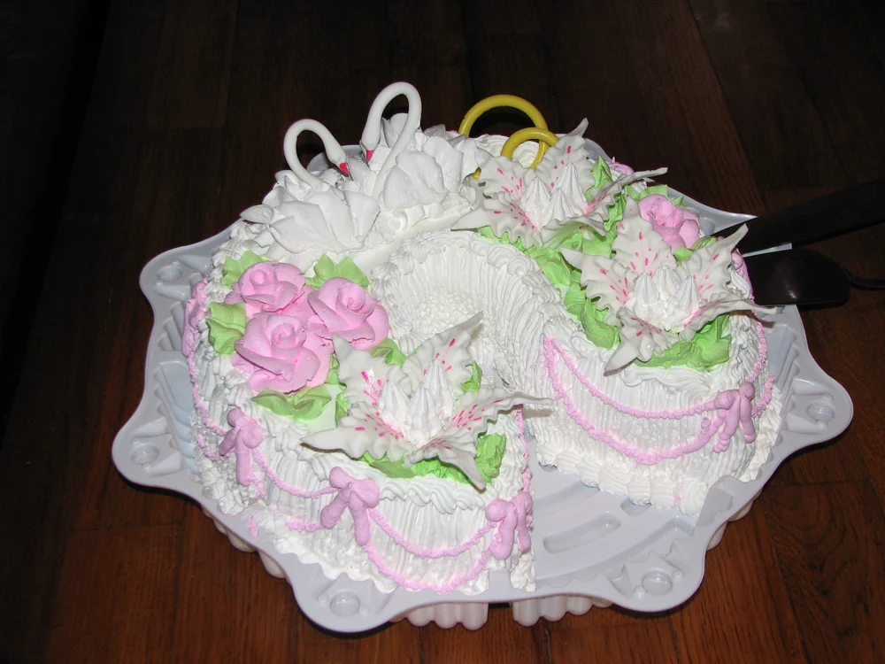 Vue aérienne du gâteau de mariage en forme de cygne montrant qu'il s'agit de deux gâteaux en forme de cœur réunis, décorés de roses passepoilées roses, de bordures ébouriffées et de feuilles vertes