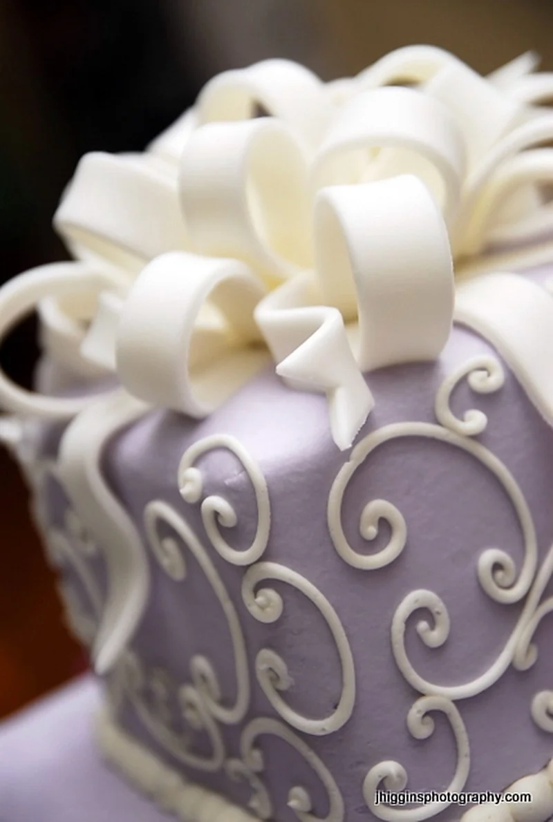 Gâteau de mariage moderne à la lavande avec des volutes de crème surpassées et un nœud en ruban en boucle dans le style Lambeth vintage