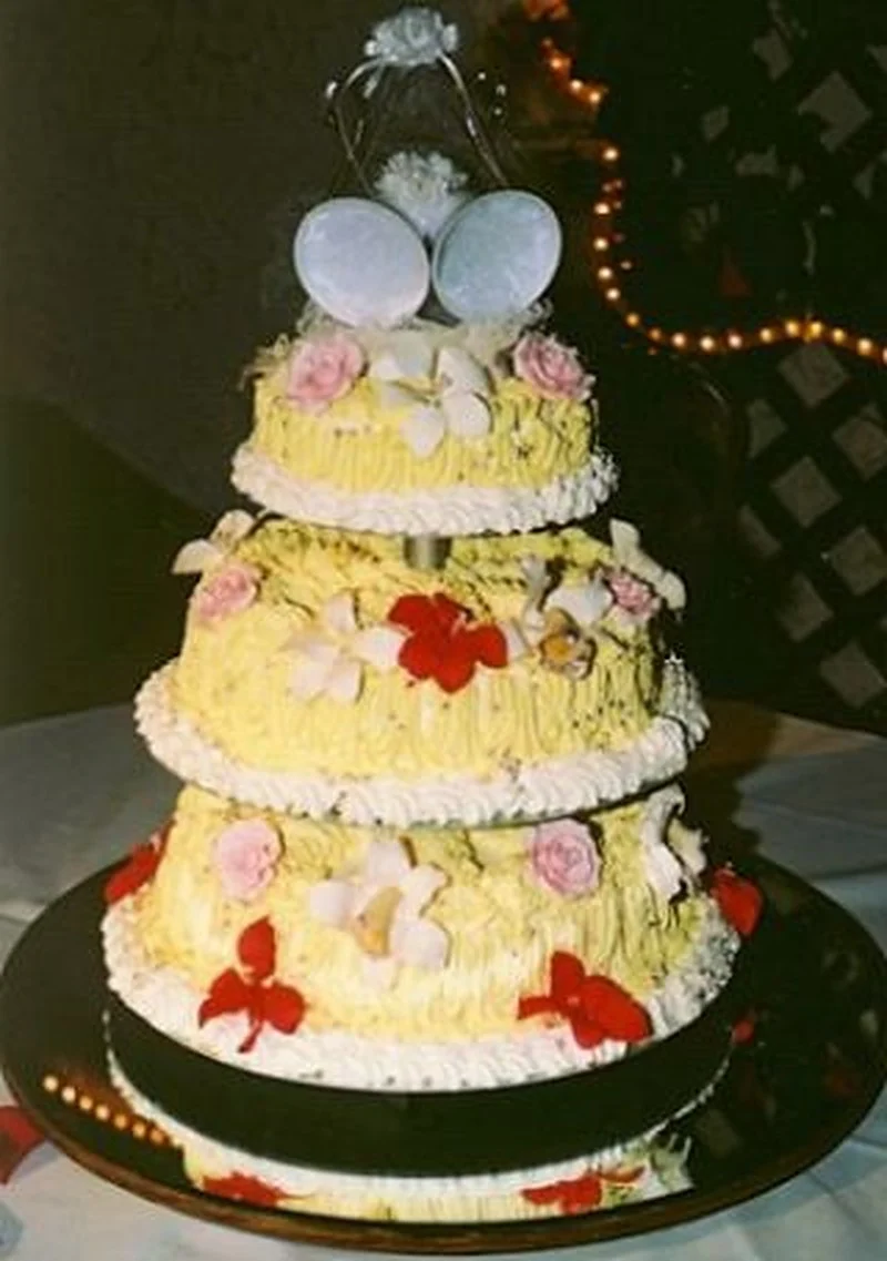 Gâteau de mariage à la crème au beurre avec glaçage jaune texturé, petites fleurs passepoilées et cloches de mariage blanches comme décoration