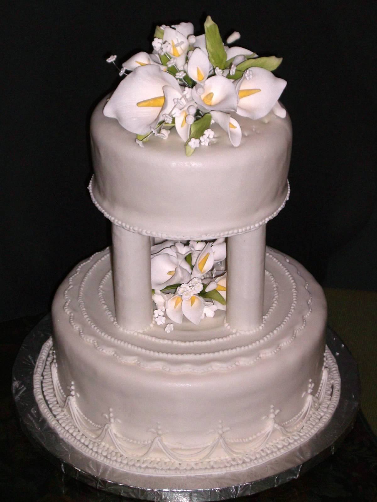 Gâteau de mariage à plusieurs niveaux avec une colonnade au niveau intermédiaire tenant des lys calla fondants entre les colonnes
