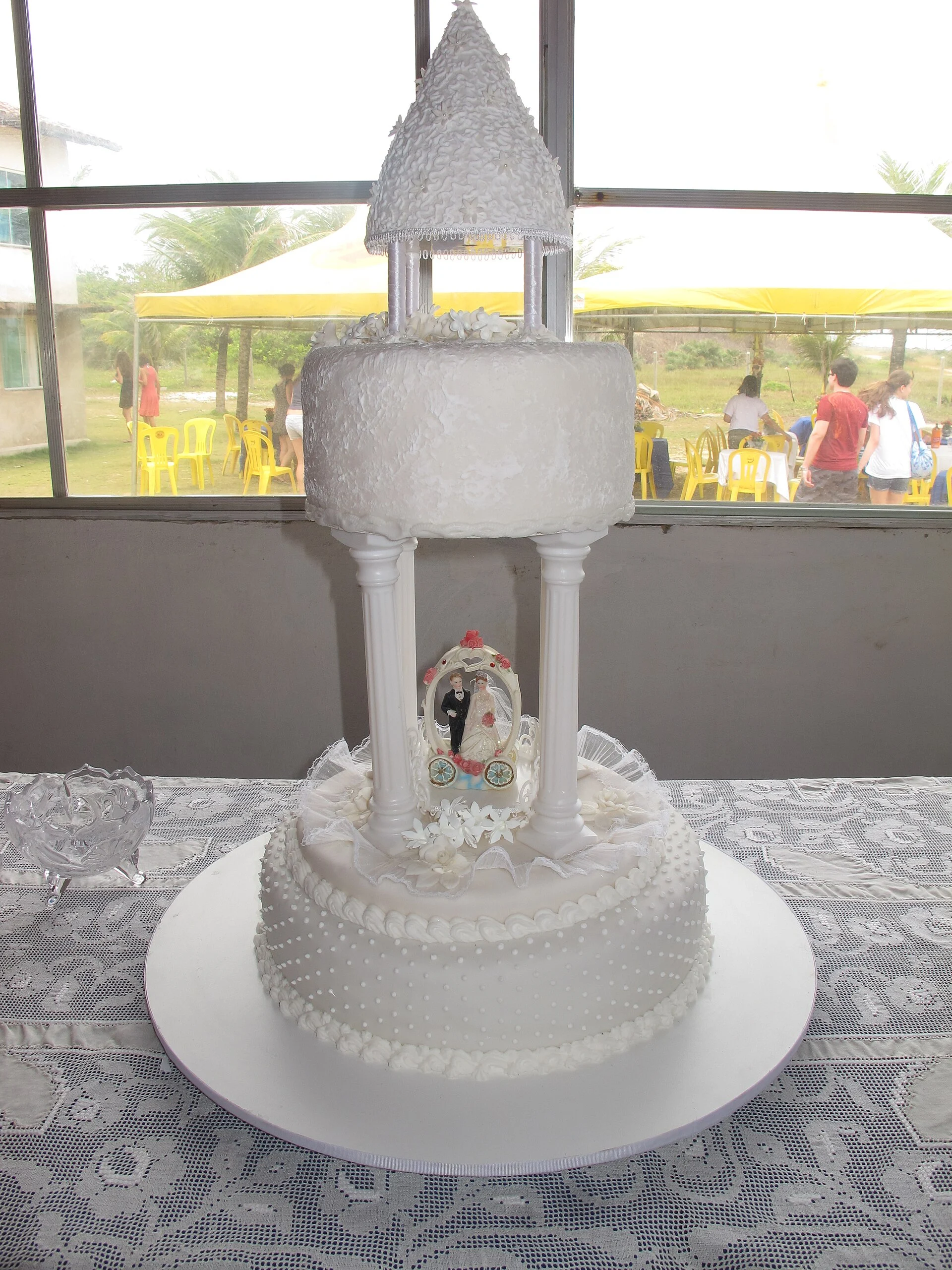 Gâteau de mariage avec un niveau supérieur de gazebo à piliers tenant une petite décoration de mariée et de marié sous son toit