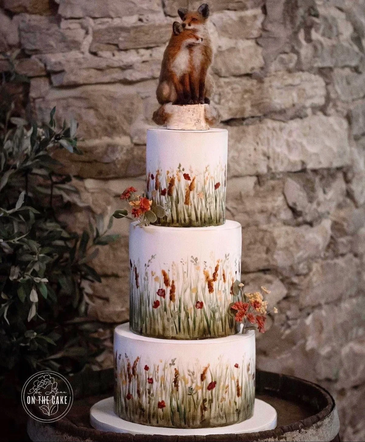 Gâteau de mariage peint avec des herbes des prairies et des fleurs sauvages, surmonté de deux renards câlins