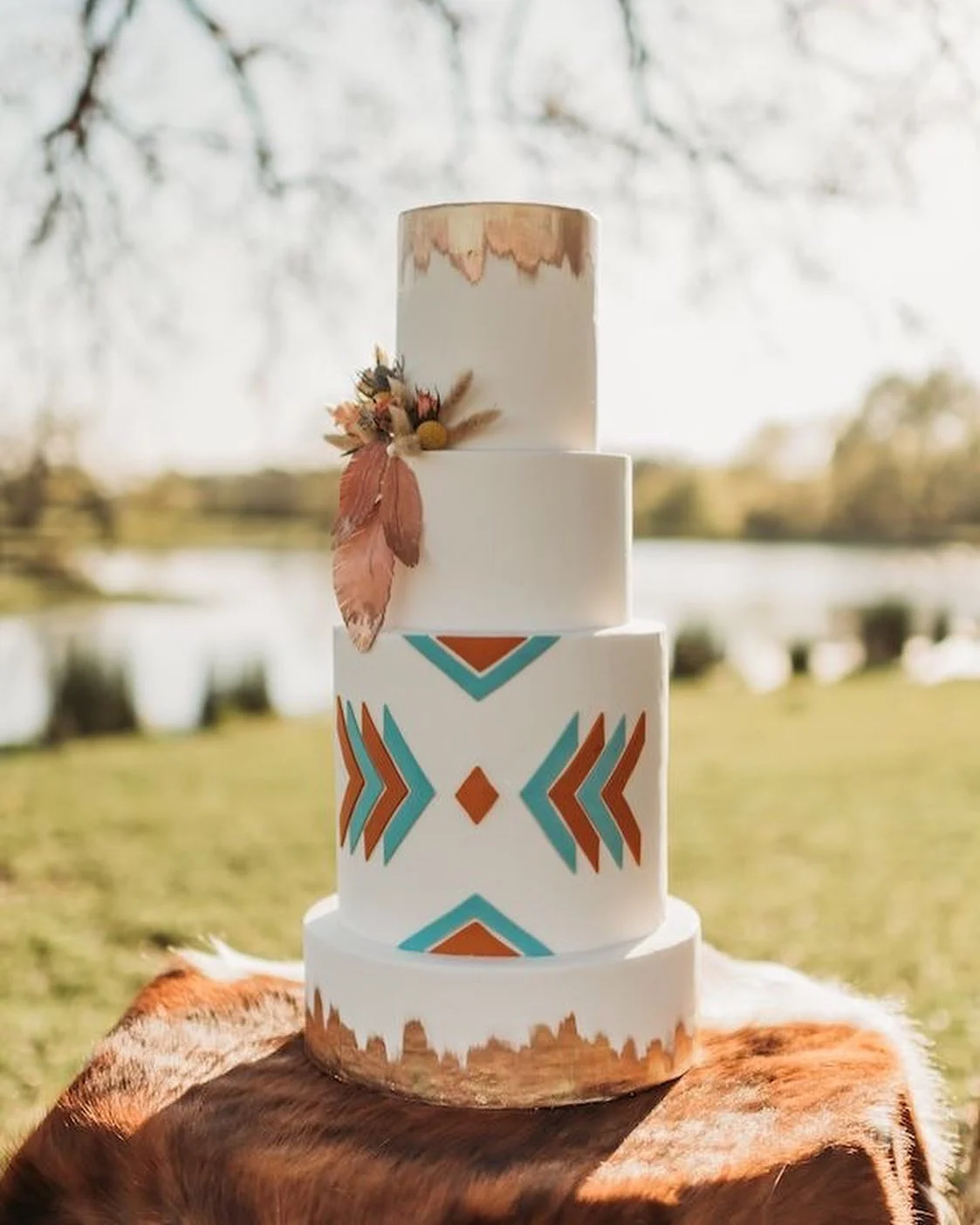 Gâteau de mariage occidental avec flèches sud-ouest turquoise et rouille et feuille d'or, présenté sur une peau de vache