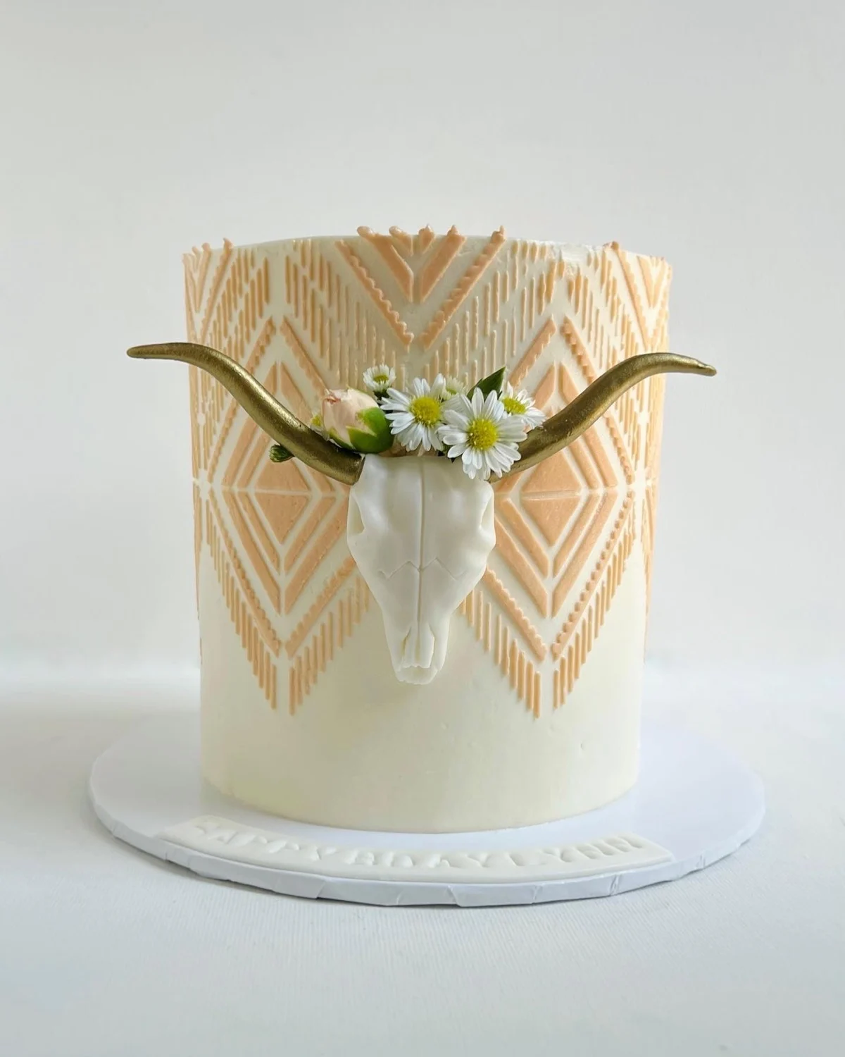 Gâteau de mariage avec un crâne de longhorn doré portant une couronne de marguerite sur un motif de pochoir du sud-ouest pêche