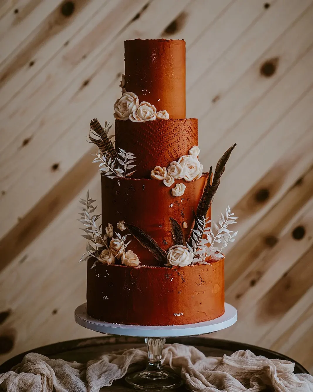 Gâteau de mariage orange brûlé à quatre niveaux avec des roses en sucre à la crème et des plumes sombres