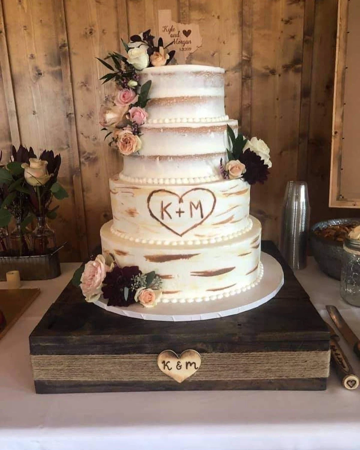 Gâteau de mariage en écorce de bouleau avec les initiales du couple sculptées dans un cœur, exposé sur un support en bois
