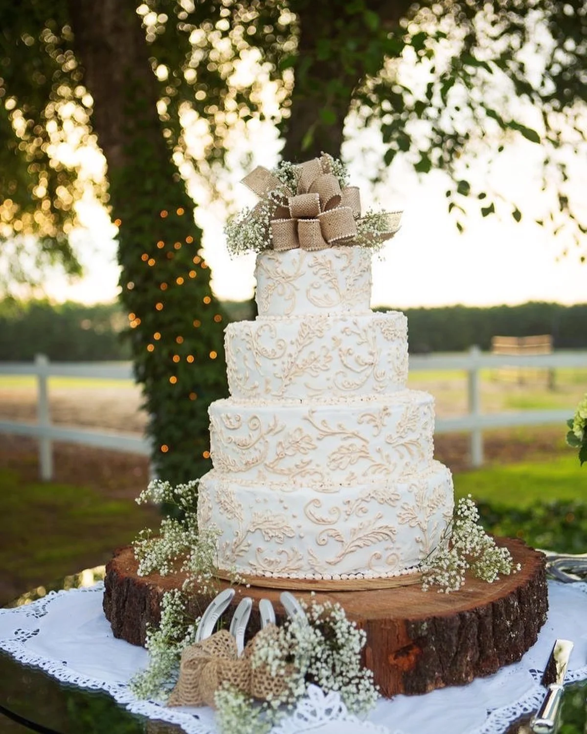 Gâteau de mariage ivoire avec passepoil à volutes, nœud en toile de jute et gypsophile sur une tranche de tronc d'arbre