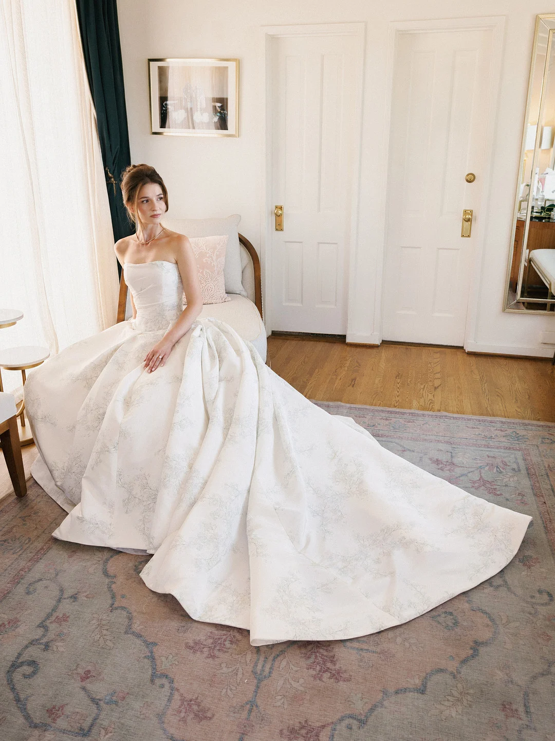Baylee assise avec sa robe de bal ivoire et sa traîne étalées sur le tapis.