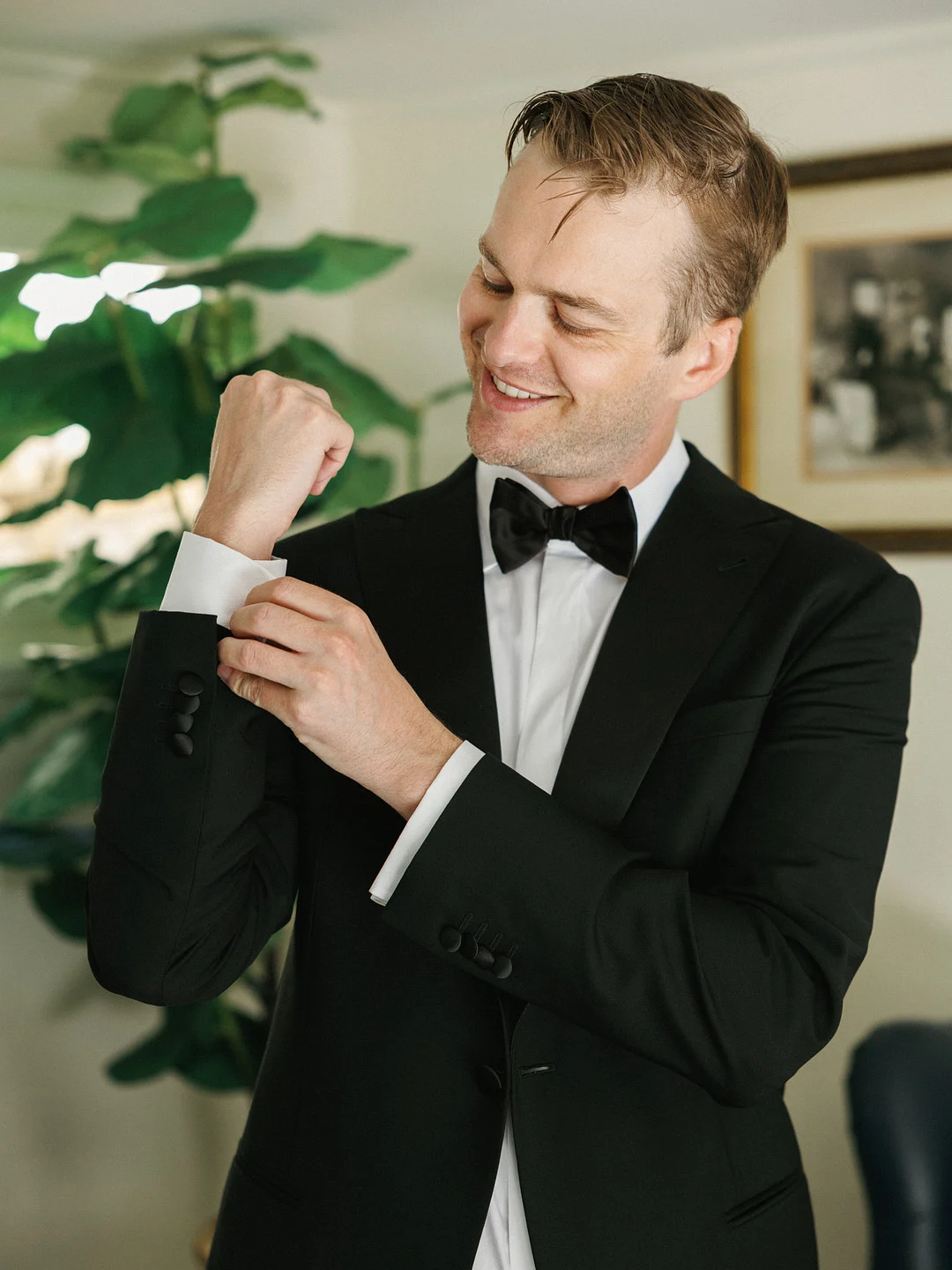 Avery souriant tout en attachant ses boutons de manchette dans un smoking noir