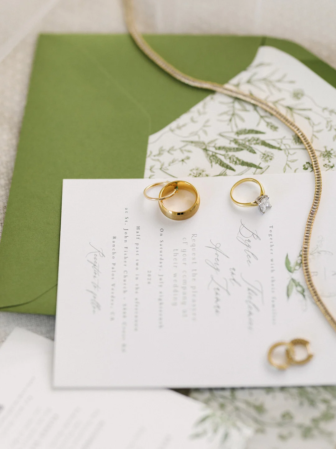 Faire-part de mariage avec enveloppe verte, collier en or et alliances du couple