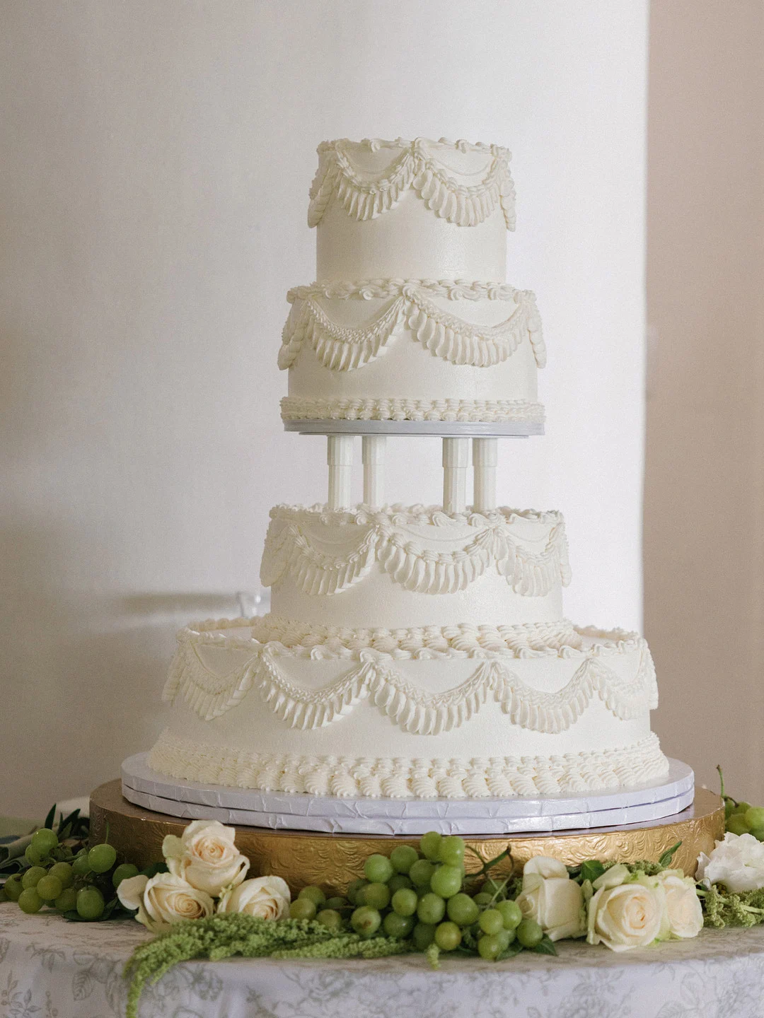 Gâteau de mariage de style Lambeth à quatre niveaux avec des guirlandes et des colonnes passepoilées sur un support doré