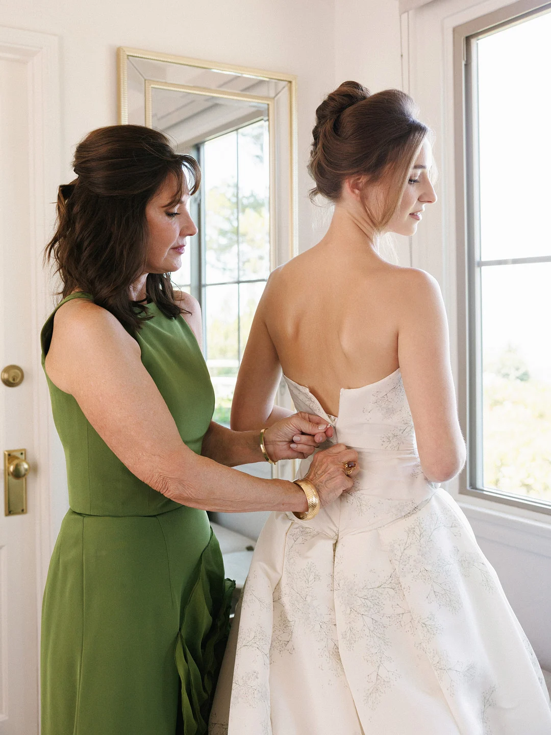La mère de Baylee en robe verte la boutonne dans sa robe de mariée
