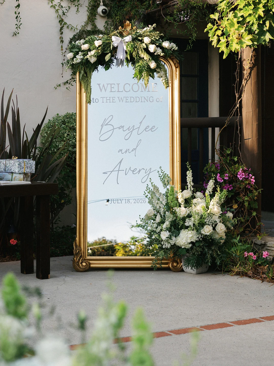 Panneau de bienvenue miroir doré entouré de fleurs blanches et vertes à la réception